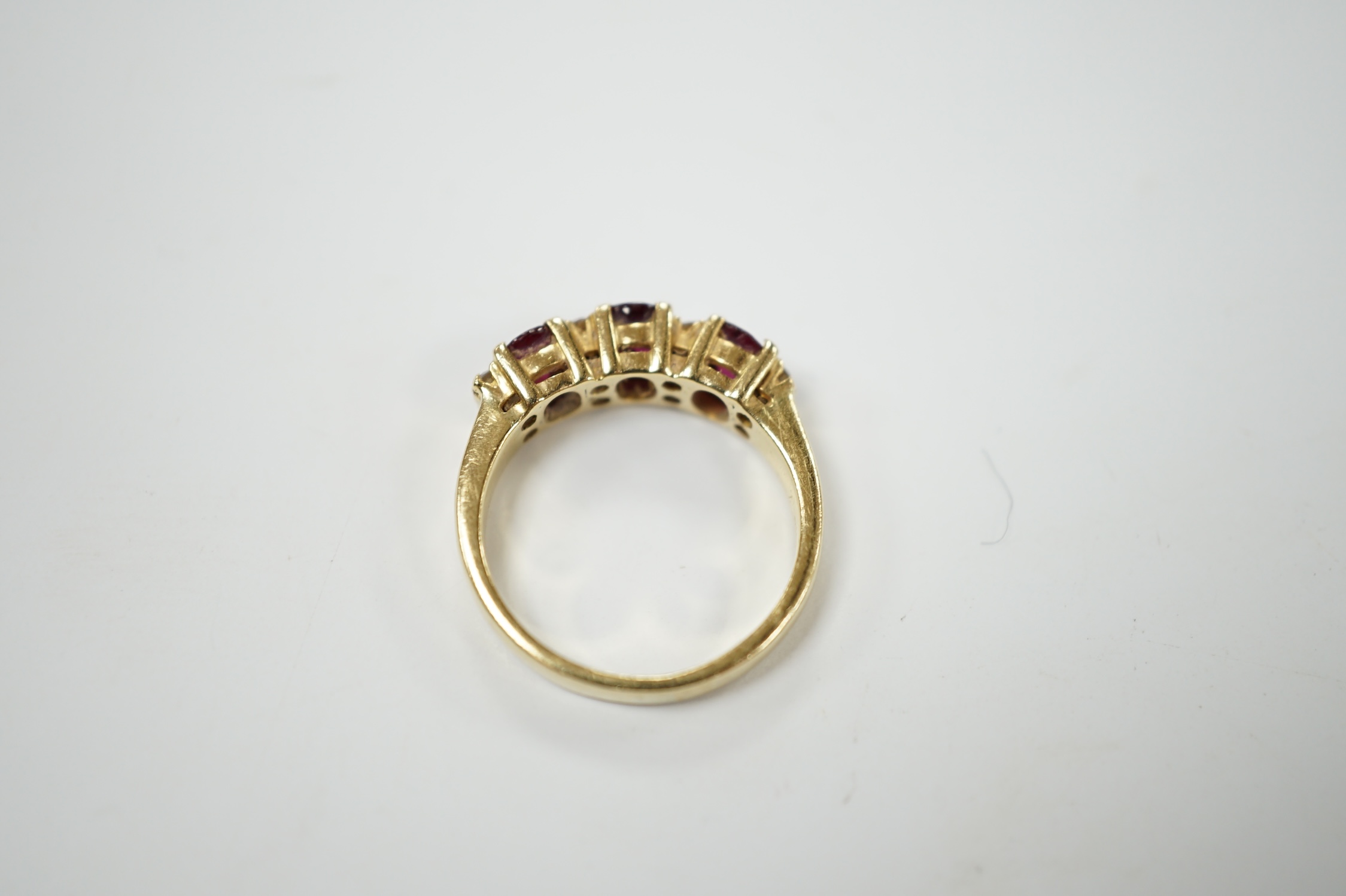 A modern yellow metal and three stone ruby set half hoop ring, with diamond chip spacers, size L, gross weight 5 grams. Condition - fair